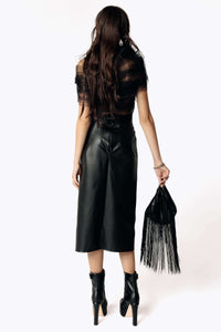 Woman wearing a black outfit with a leather skirt and holding a black fringe bag on a white background