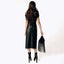 Woman wearing a black outfit with a leather skirt and holding a black fringe bag on a white background