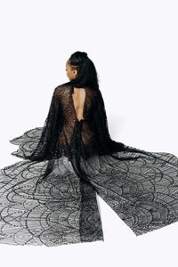 Back view of Cameron wearing the Azrael Black Winged Sleeve Maxi Dress, a full-length black mesh dress showing a deep plunging back while sitting on the floor with a long mesh train from SCATHED's Fall Winter 2025 Reaper collection.