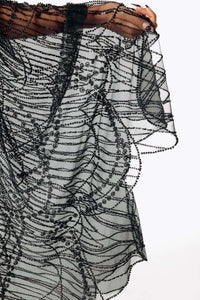 Macro view of Cameron wearing the Azrael Black Winged Sleeve Maxi Dress, a full-length black mesh dress from SCATHED's Fall Winter 2025 Reaper collection, extends her arm showing the draping bat winged sleeves.