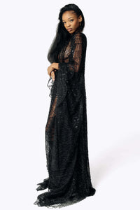 Side view of Cameron wearing the Azrael Black Winged Sleeve Maxi Dress, a full-length black mesh dress that flares out from the hips with her arms crossed at the waist from SCATHED's Fall Winter 2025 Reaper collection.