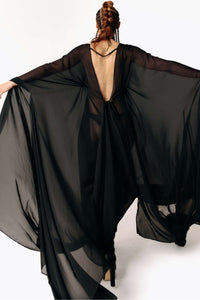 Back view of Caitlin stepping away from camera while wearing the Dark Angel Chiffon Sheer Maxi Dress with billowing draping wide sleeves from SCATHED's Fall Winter 2025 Reaper collection.
