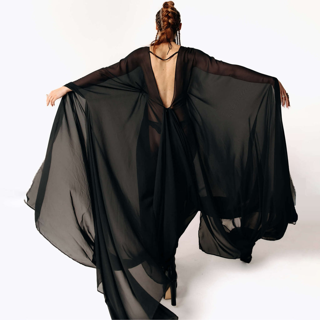 Back view of Caitlin stepping away from camera while wearing the Dark Angel Chiffon Sheer Maxi Dress with billowing draping wide sleeves from SCATHED's Fall Winter 2025 Reaper collection.
