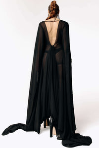 Back view of Caitlin facing away from  camera while wearing the Dark Angel Chiffon Sheer Maxi Dress with billowing draping floor-length sleeves from SCATHED's Fall Winter 2025 Reaper collection.