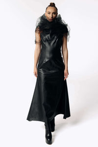 Front view of Caitlin wearing the Kalma Cactus Leather Maxi Dress, a full-length black leather dress that flares out from the hips with the Wraith Black Tulle Collar from SCATHED's Fall Winter 2025 Reaper collection. Caitlin also wears high-heeled black platformed ankle boots.