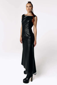 Side view of Caitlin wearing the Kalma Cactus Leather Maxi Dress, a full-length black leather dress that flares out from the hips from SCATHED's Fall Winter 2025 Reaper collection. Caitlin also wears high-heeled black platformed ankle boots.