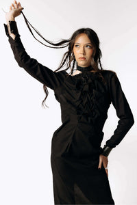 Frontal view of Eliza wearing the Mors Black Cotton Dress with ruffling in the chest from SCATHED's Fall Winter 2025 Reaper collection, while playing with her hair and looking off to the left.
