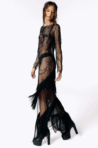 Side portrait view of Eliza wearing the Morta Beaded Cross Fringe Dress featuring intricate beaded embellishments and sheer layered with fringe from SCATHED's Fall Winter 2025 Reaper collection. Eliza also wears high-heeled platform black ankle boots.