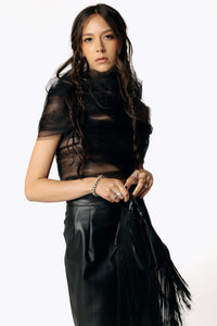 Side portrait view of Eliza wearing the sheer Motte Tulle Cloud blouse and Grim Cactus Leather Skirt from SCATHED's Fall Winter 2025 Reaper collection.