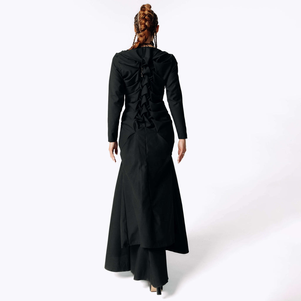 Back view of Caitlin with braided hair wearing the Nox Black Cotton Skeleton Dress with a ruffled spinal details from SCATHED's Fall Winter 2025 Reaper collection.