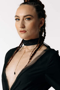 Macro view of Caitlin  with braided hair wearing the Nox Black Cotton Skeleton Dress with a deep plunging neckline from SCATHED's Fall Winter 2025 Reaper collection.