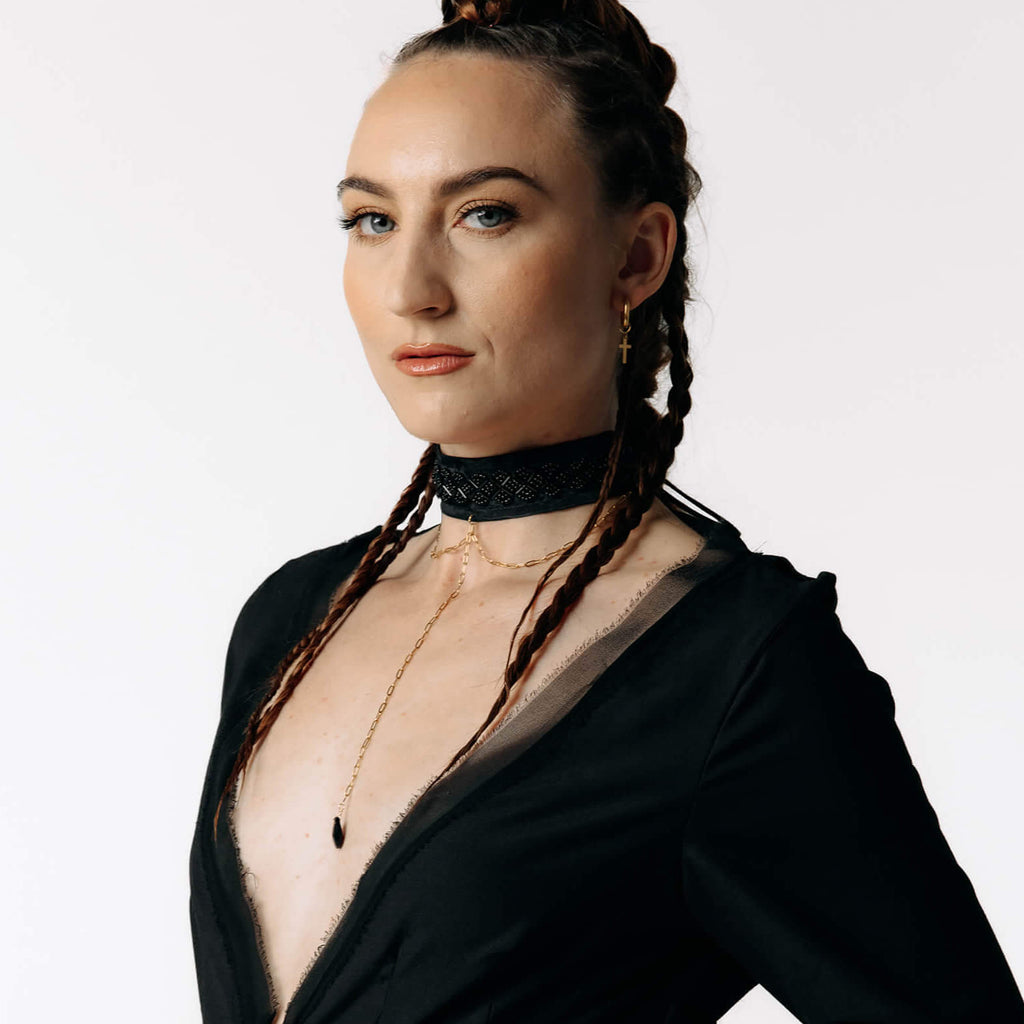 Macro view of Caitlin  with braided hair wearing the Nox Black Cotton Skeleton Dress with a deep plunging neckline from SCATHED's Fall Winter 2025 Reaper collection.