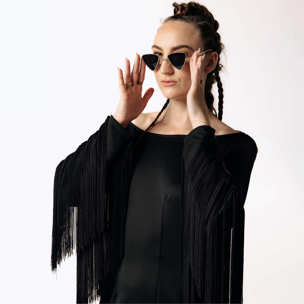 Close-up frontal view of Caitlin wearing the Revenant Black Dress with fringed sleeves awhile putting on Vex Sunglasses from SCATHED's Fall Winter 2025 Reaper collection.