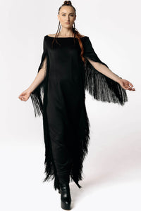 Frontal view of Caitlin stepping towards camera while wearing the Revenant Black Dress with fringed sleeves and a high thigh-slit from SCATHED's Fall Winter 2025 Reaper collection.