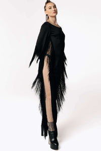 Side view of Caitlin stepping towards camera while wearing the Revenant Black Dress with fringed sleeves and a high thigh-slit from SCATHED's Fall Winter 2025 Reaper collection.