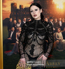 Samantha Lubrano wears the Morta Beaded Gown for SCATHED's F/W25 Reaper Collection to the Downtown Abbey premiere event while standing in front of a poster depicting scenes from the show. Image Credit: Arturo Holmes, Getty Images