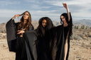 Three models in black robes standing in a desert landscape wearing the FW25 Collection, Reaper