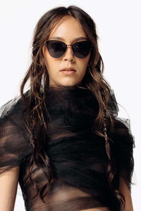 Image of Eliza wearing the Venin Black sunglasses while facing the camera wearing the black sheer Mot Tulle Cloud Blouse from SCATHED's Fall Winter 2025 Reaper collection.