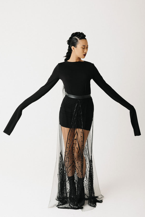 Video of model showing black long sleeve shirt styled with a sheer hand beaded skirt showing front side and back view