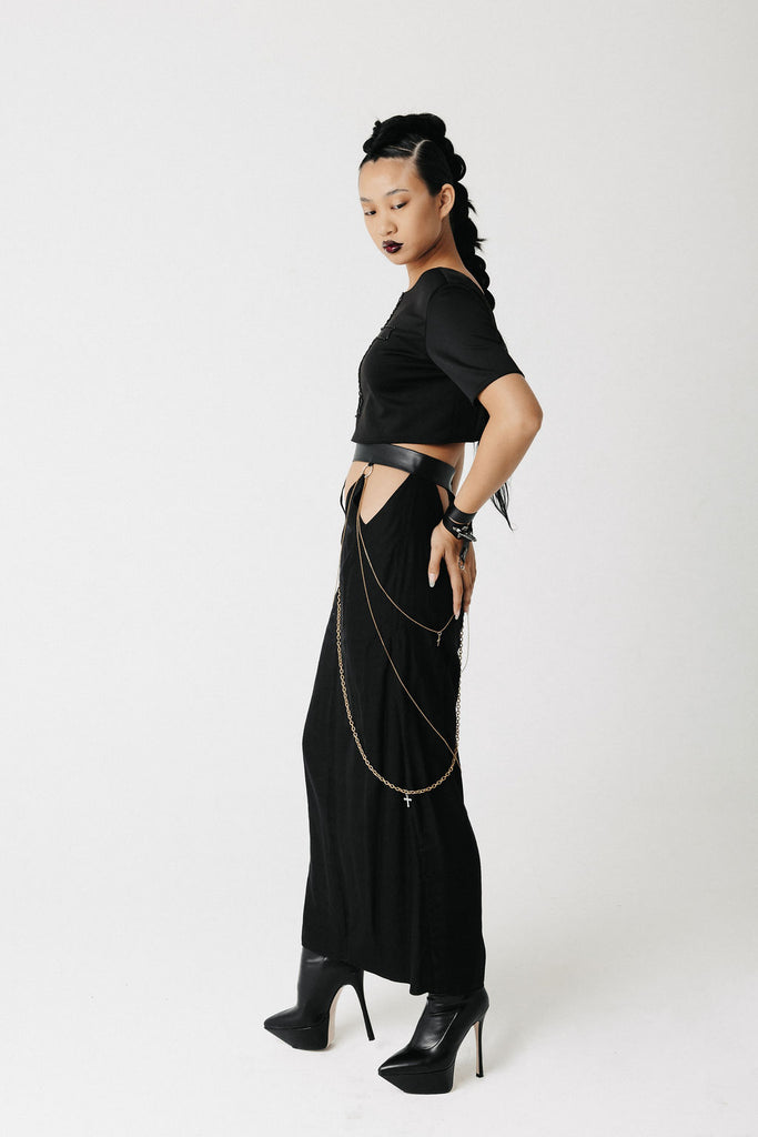 Model wears cut out skirt with gold chains and gold cross charms as details and a crop t shirt. Shows front, side, and back views with details