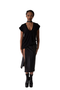 A model stands in a studio wearing a black t-shirt top with short cap sleeves and low v neck, a matching black skirt with a front slit, and black ankle boots.