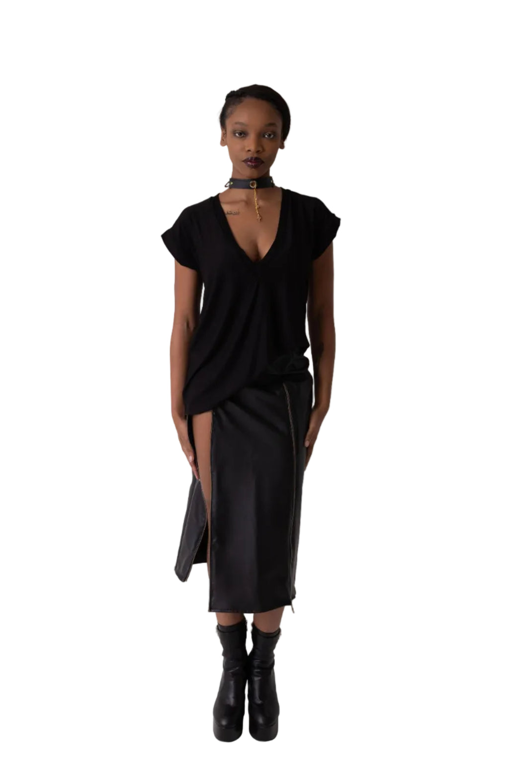 A model stands in a studio wearing a black t-shirt top with short cap sleeves and low v neck, a matching black skirt with a front slit, and black ankle boots.