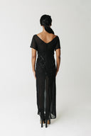Model wearing black hand-beaded sheer chiffon gown, full length, with platform boots. Showing back of dress.