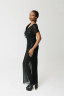 Model wearing black hand-beaded sheer chiffon gown, full length, with platform boots. Showing side view of dress.