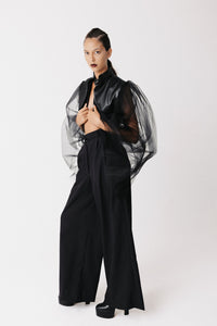 Model wearing black cactus leather cropped bolero jacket with sheer tulle balloon sleeves, arms outstretched, side view