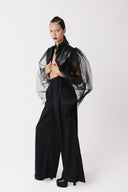 Model wearing black cactus leather cropped bolero jacket with sheer tulle balloon sleeves, arms outstretched, side view