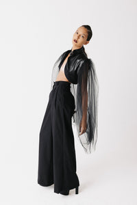 Side view of model wearing black cactus leather bolero jacket with sheer tulle sleeves and wide-leg trousers