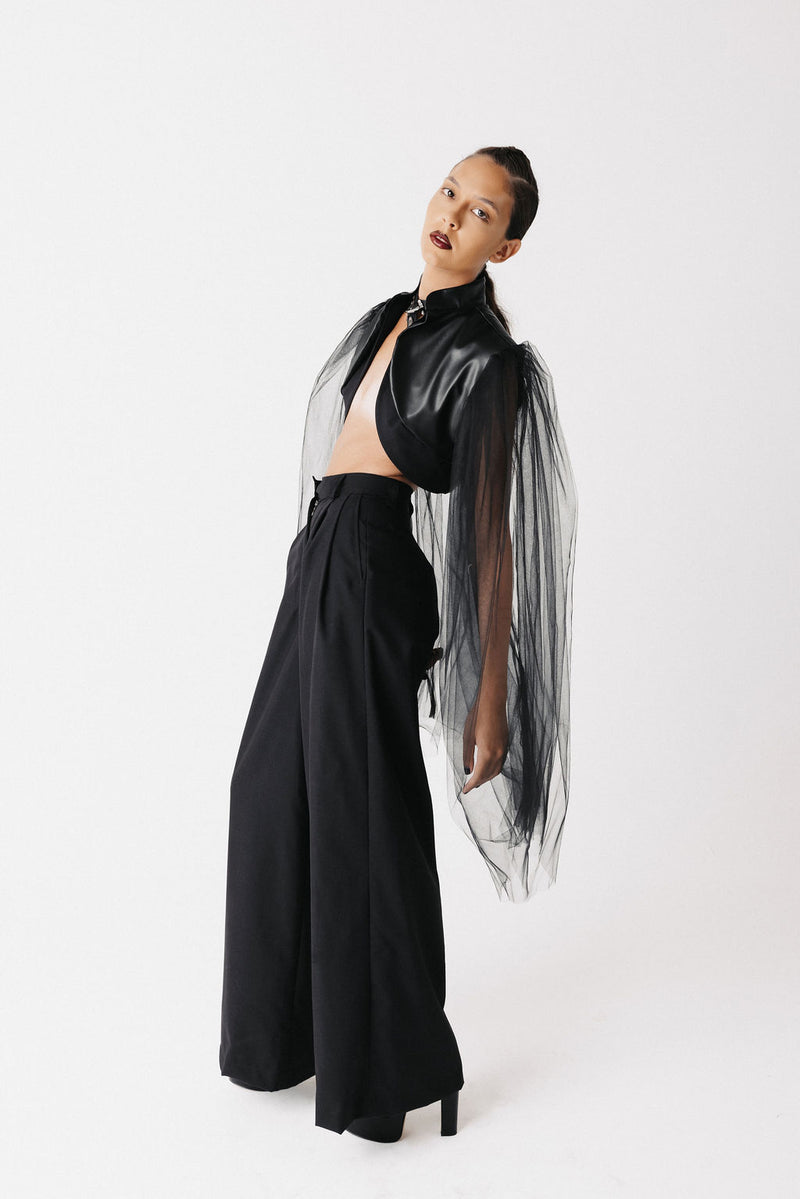 Side view of model wearing black cactus leather bolero jacket with sheer tulle sleeves and wide-leg trousers