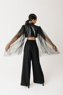 Back view of model wearing black cactus leather bolero jacket with sheer tulle sleeves and wide-leg trousers
