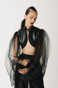 Model wearing black cactus leather cropped bolero jacket with sheer tulle balloon sleeves, arms outstretched, front view close up