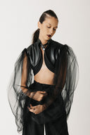 Model wearing black cactus leather cropped bolero jacket with sheer tulle balloon sleeves, arms outstretched, front view close up