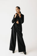 Model wearing the Mourner Shirt, a cropped black button-up in organic bamboo cotton, worn open over trousers