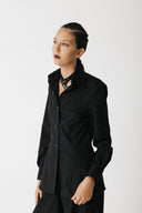 A model wearing the mourner black long-sleeve button-up shirt with a relaxed, slightly oversized fit, styled with a patterned black neck scarf, set against a plain light gray studio background.