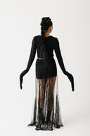 Model wearing black jersey top with extra-long sleeves and boat neckline, styled with sheer skirt back view
