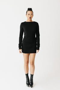 Model wearing black jersey top with extra-long sleeves and boat neckline, styled as a mini dress front view