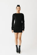 Model wearing black jersey top with extra-long sleeves and boat neckline, styled as a mini dress front view