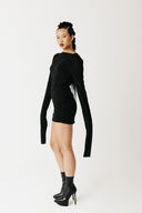 Model wearing black jersey top with extra-long sleeves and boat neckline, styled as a mini dress side view
