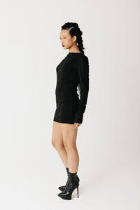 Model wearing black jersey top with extra-long sleeves and boat neckline, styled as a mini dress side view
