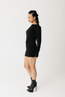 Model wearing black jersey top with extra-long sleeves and boat neckline, styled as a mini dress side view