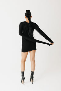 Model wearing black jersey top with extra-long sleeves and boat neckline, styled as a mini dress back view