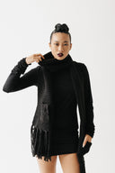 Model wearing chunky oversized black tassel scarf with visible patch pocket and fringe trim