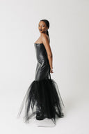 A model wearing a black strapless cactus leather corset-style dress and a voluminous black tulle mermaid skirt, standing against a plain light gray studio background.