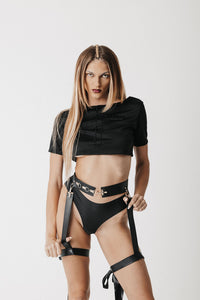 Front view of model wearing the Bridle Harness, a cactus leather waist and leg harness with gold hardware, over a cropped tee and underwear