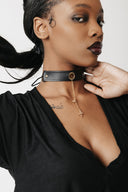 A close-up of a model wearing a black leather choker necklace with a gold-tone flower pendants and chain.