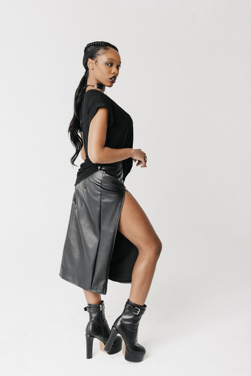 Side view of model wearing the Void Tee, a black jersey V-neck tee with a draped asymmetric hem, styled with a leather skirt sold separately
