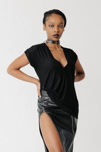 Front view of model wearing the Void Tee, a black jersey V-neck tee with a draped asymmetric hem, styled with a leather skirt sold separately